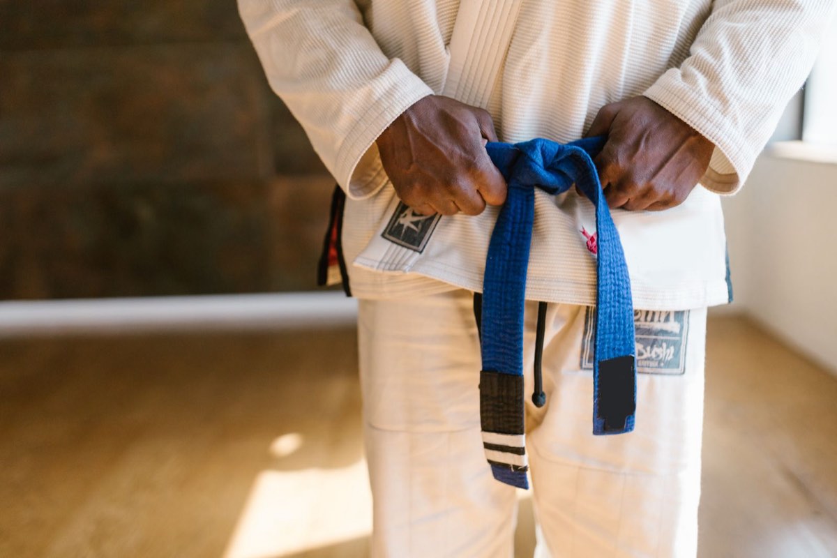 A Brazilian Jiu-Jitsu practitioner tying a blue belt with stripes
