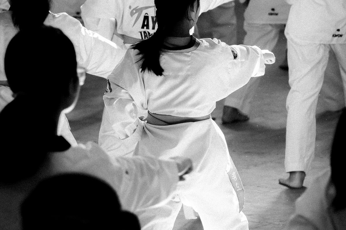 A full karate class of students in white uniforms practising together in a training hall