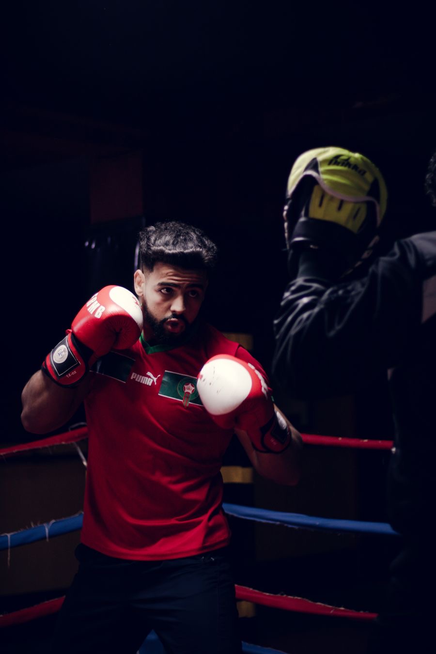 An adult boxer in red gloves training with a coach in the ring