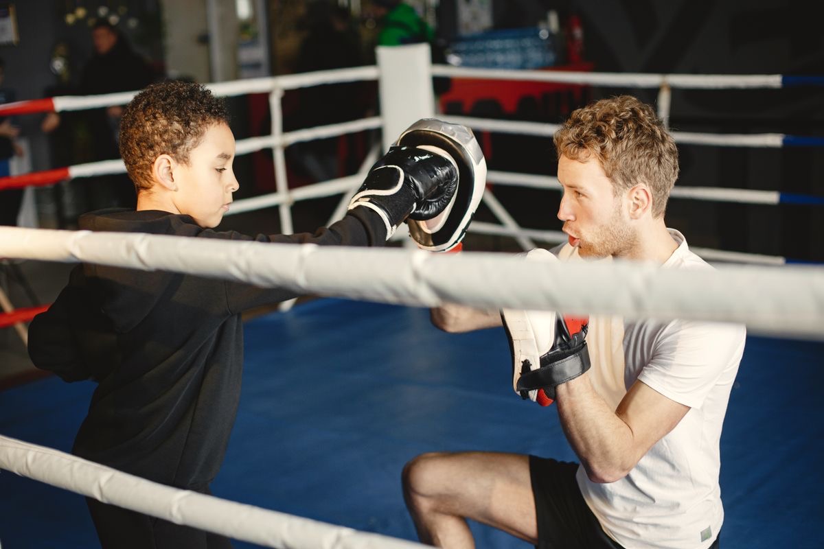 A boxing coach holding focus mitts for a young boxer in the ring