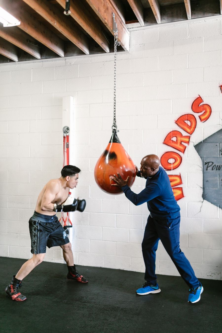 A boxing coach guiding a boxer through punches on a hanging bag