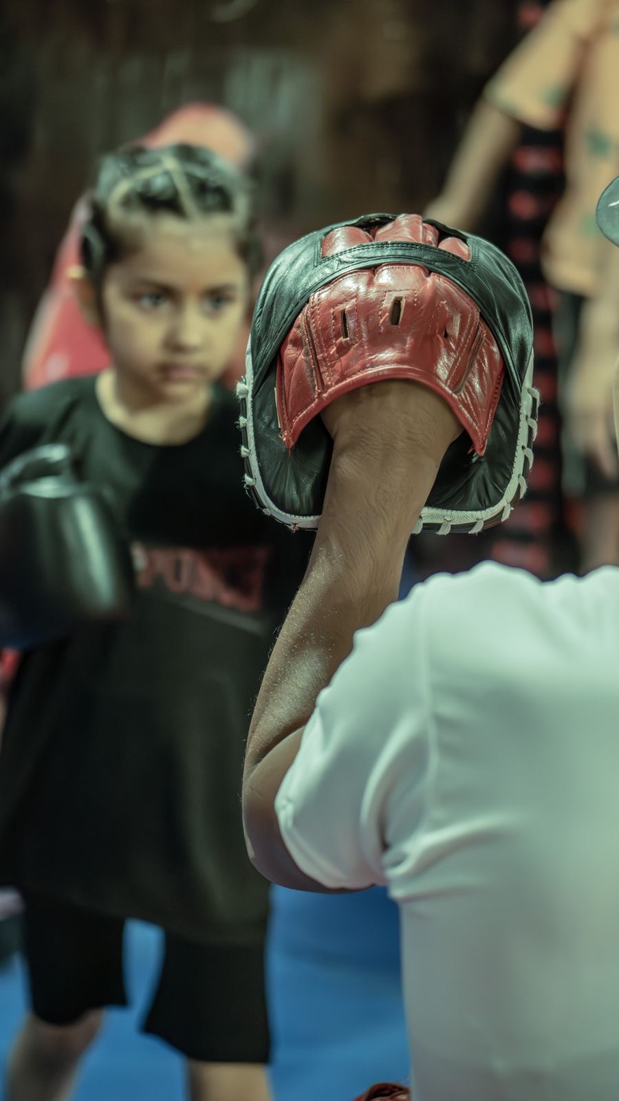 A young girl in boxing gloves training with a coach holding mitts