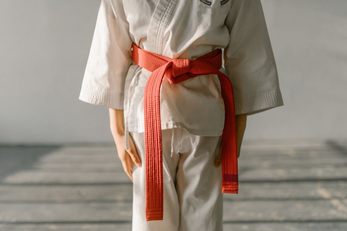 An adult student in a white uniform tying an orange belt
