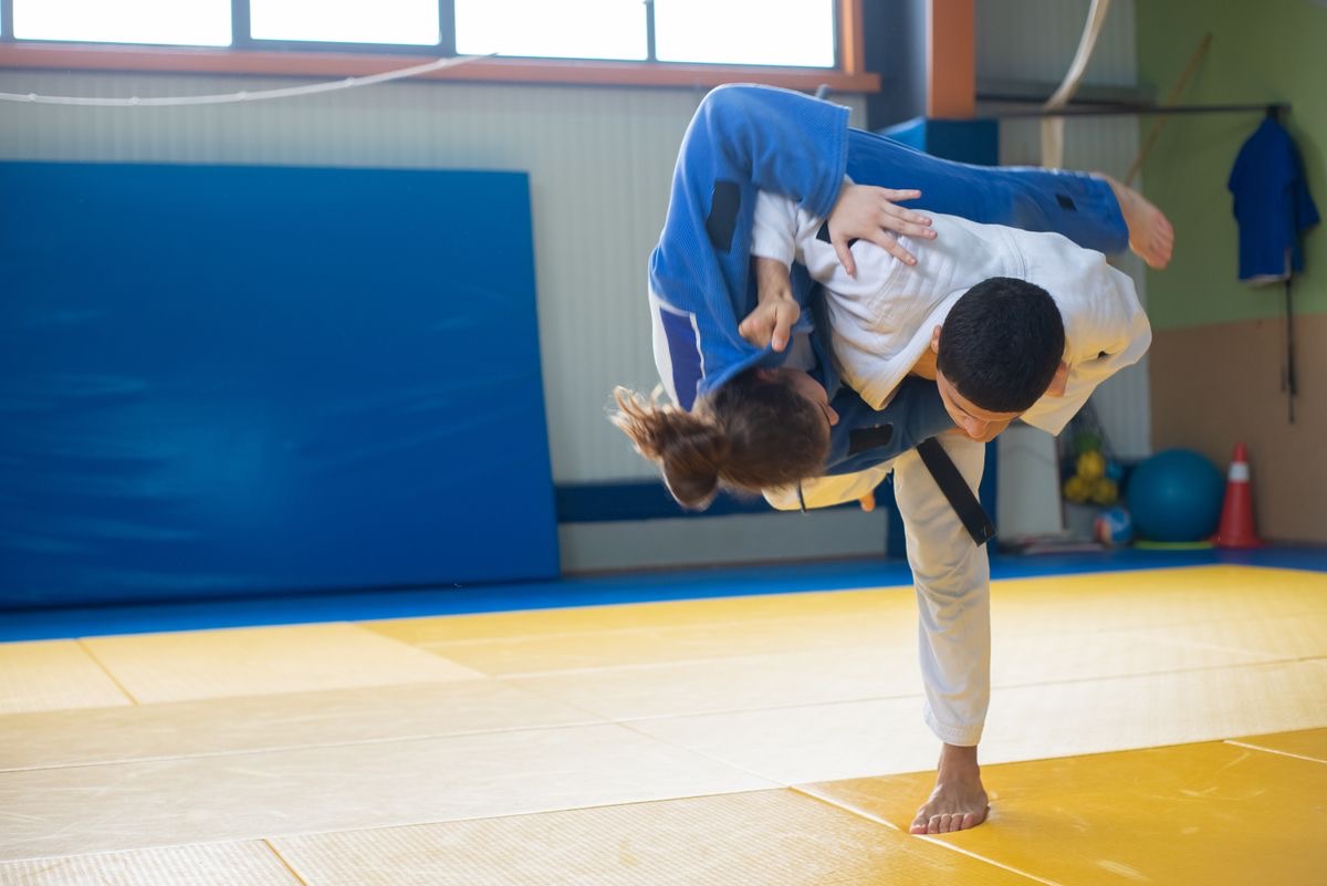 A judoka in a white judogi throwing a partner in a blue judogi onto the tatami