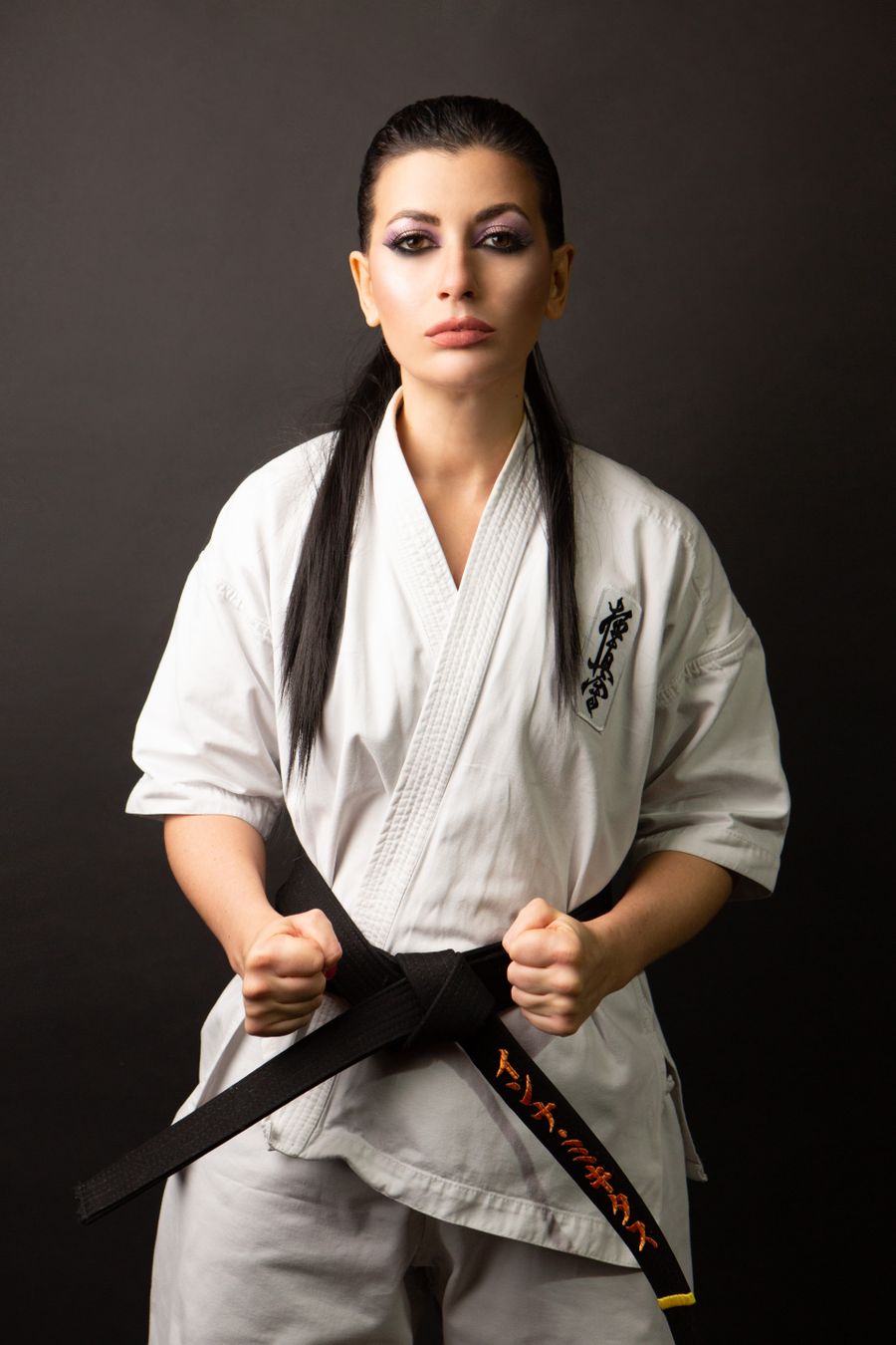 A karate black belt in a white gi holding the ends of her belt