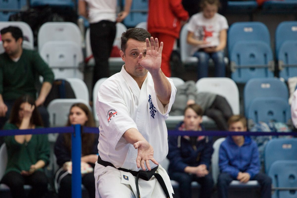 A karate master in a white gi performing a kata at a karate competition