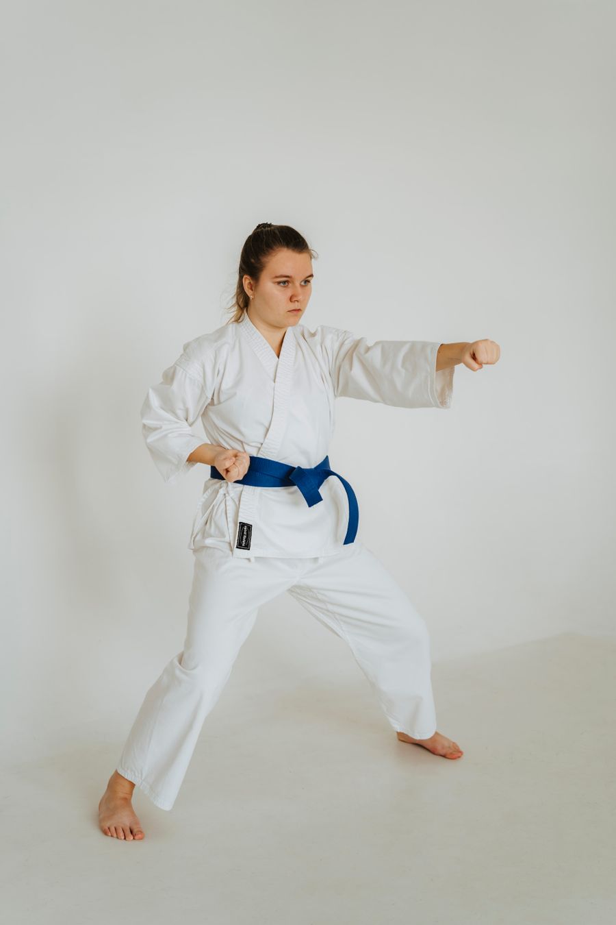 A karate student in a white gi and blue belt performing a kata stance