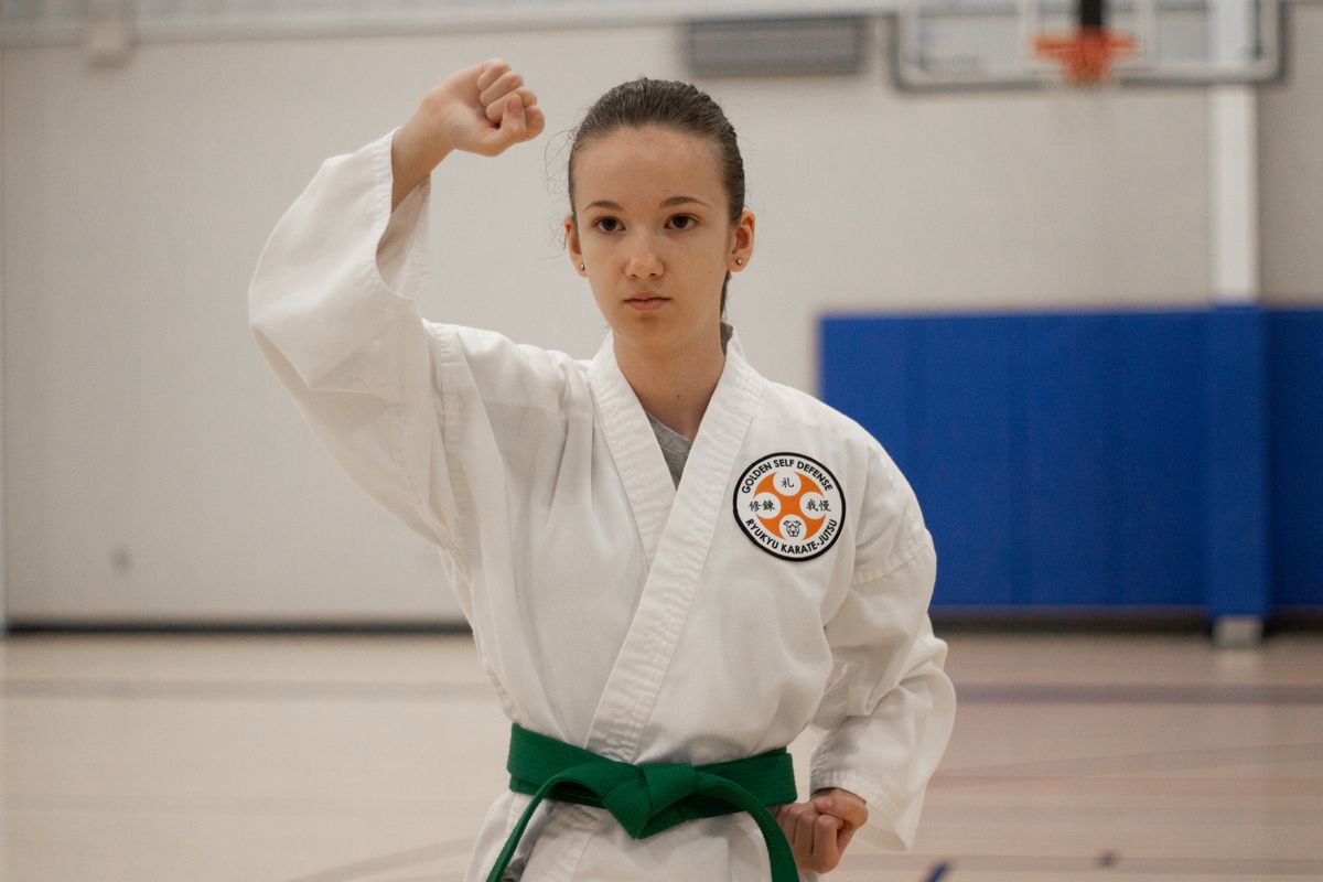 A young karate student in a white gi and green belt in a fighting stance