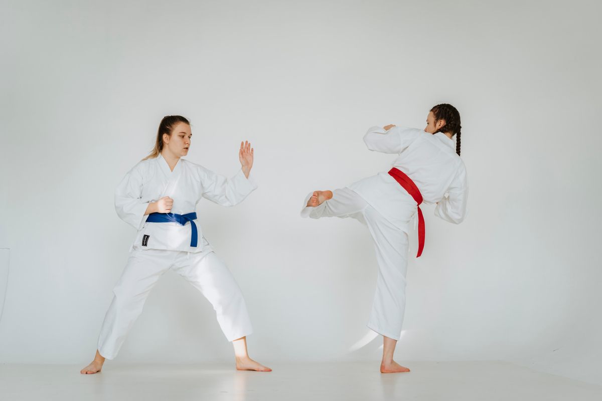 Two karate students in white gis practicing kumite, one throwing a kick