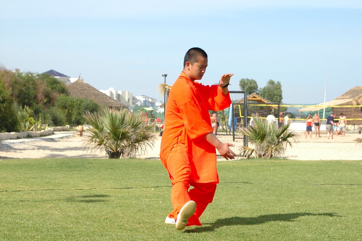 A Kung Fu practitioner in orange Shaolin-style robes training outdoors