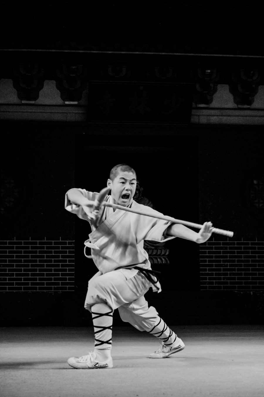 A Shaolin practitioner in traditional uniform performing a staff form