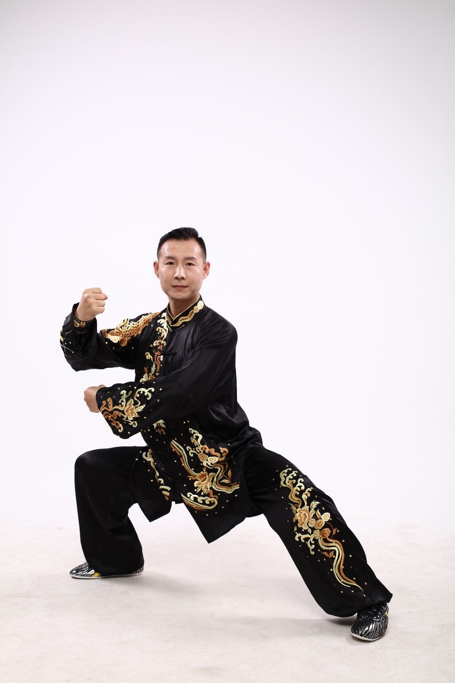 A Kung Fu practitioner in a black uniform with gold dragon embroidery holding a low stance