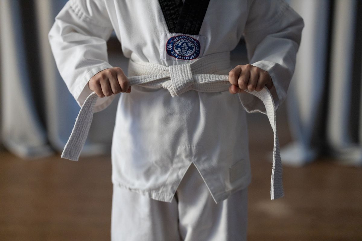 A Taekwondo student in a white dobok with black trim tying a white belt