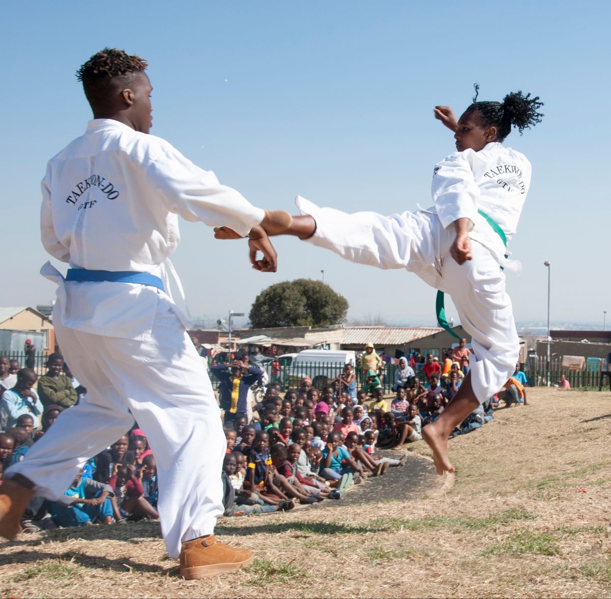 Two Taekwondo students performing a flying kick at an outdoor demonstration