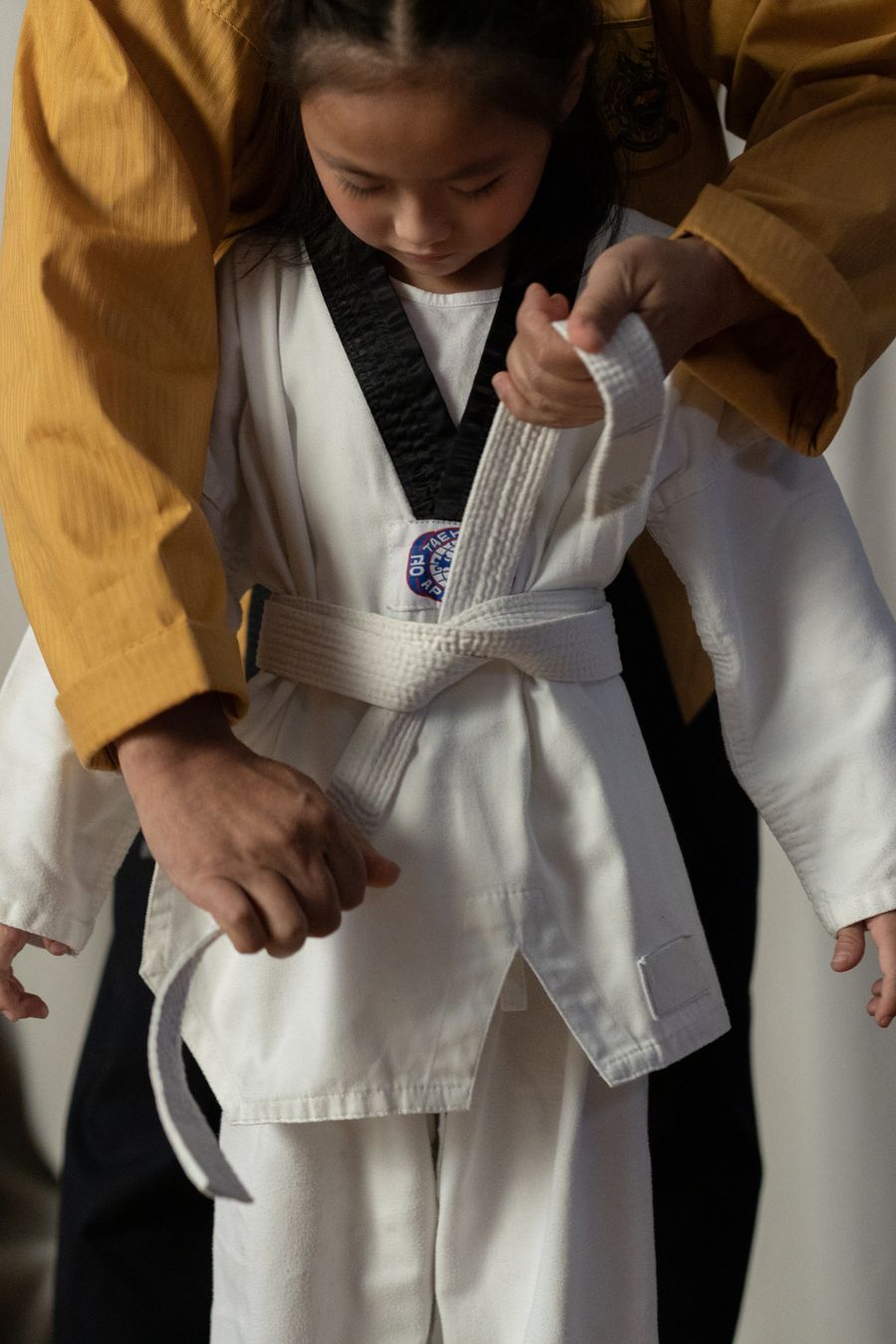 A Taekwondo instructor tying the belt of a young student in a dobok