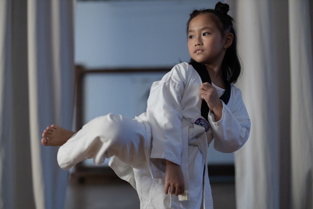 A young girl in a Taekwondo dobok practicing a kick