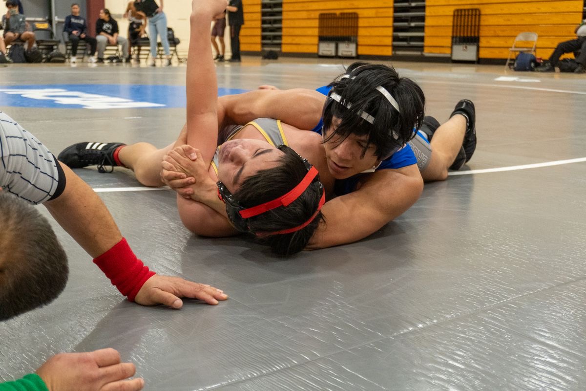 Two scholastic wrestlers in headgear working for control on the mat