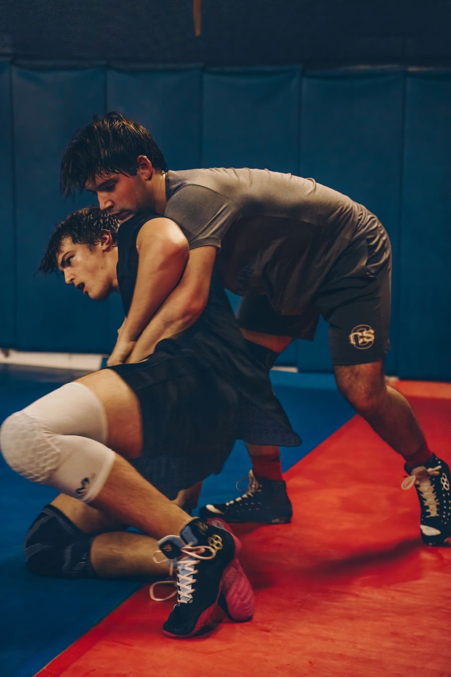 A wrestler driving in on a leg attack during practice on a wrestling mat