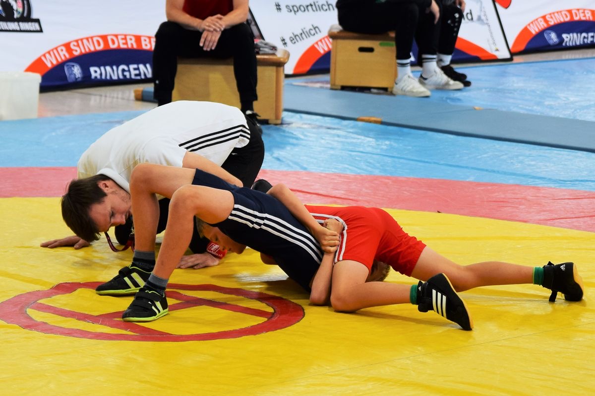 Two young wrestlers in a match on a wrestling mat with a coach watching